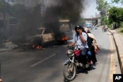 A motorcyclist drives past a burning vehicle set on fire by angry supporters of Pakistan's former Prime Minister Imran Khan, in Lahore, Pakistan, May 11, 2023.