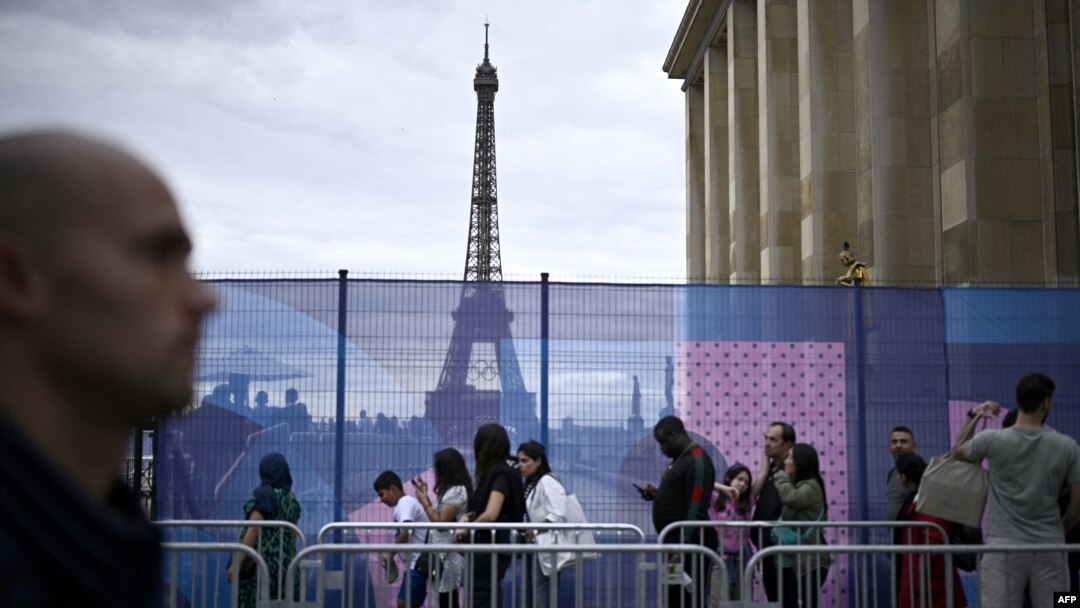 Pengunjung berjalan melewati pembatas di Trocadero dengan latar belakang Menara Eiffel di Paris, 16 Juli 2024. (JULIEN DE ROSA / AFP)