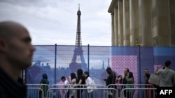 Pengunjung berjalan melewati pembatas di Trocadero dengan latar belakang Menara Eiffel di Paris, 16 Juli 2024. (JULIEN DE ROSA / AFP)