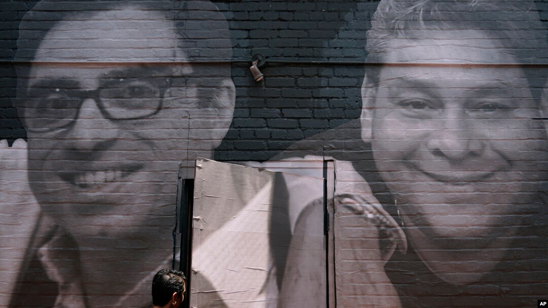 Seorang perempuan melangkah melewati pintu bergambar mural warga AS yang ditahan di luar negeri,di kawasan Georgetown, Washington, Rabu, 20 Juli 2022. Siamak Namazi (kiri) ditahan di Iran sejak 2015 dan Jose Angel Pereira (kanan), dipenjara di Venezuela sejak 2017.