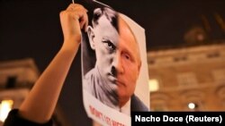 Persona sostiene una pancarta con los rostros unidos de un retrato de Vladimir Putin y el dictador nazi Adolf Hitler durante una protesta en Barcelona, España, el 24 de febrero de 2022.