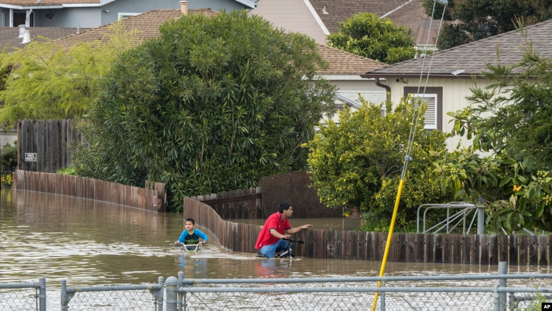 A boy and a man ride bicycles through floodwaters in Watsonville, California, March 11, 2023. 