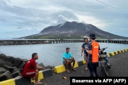 Seorang anggota Basarnas berbincang dengan warga di Sitaro, Sulawesi Utara, dengan latar belakang gunung berapi Gunung Ruang yang mengeluarkan asap. (Foto: Basarnas via AFP)
