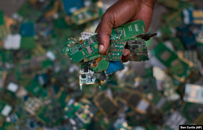 FILE - In this photo taken Monday, Aug. 18, 2014, a worker gathers handfuls of cellphone printed circuit boards from a pile to put in a sack for recycling, at the East African Compliant Recycling facility in Machakos, near Nairobi, in Kenya. (AP Photo/Ben Curtis, File)