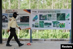 Seorang petugas keamanan melintas di depam papan informasi di titik nol wilayah pembangunan Ibu Kota Nusantara, di Sepaku, Kalimantan Timur, 8 Maret 2023. (Foto: Willy Kurniawan/Reuters)