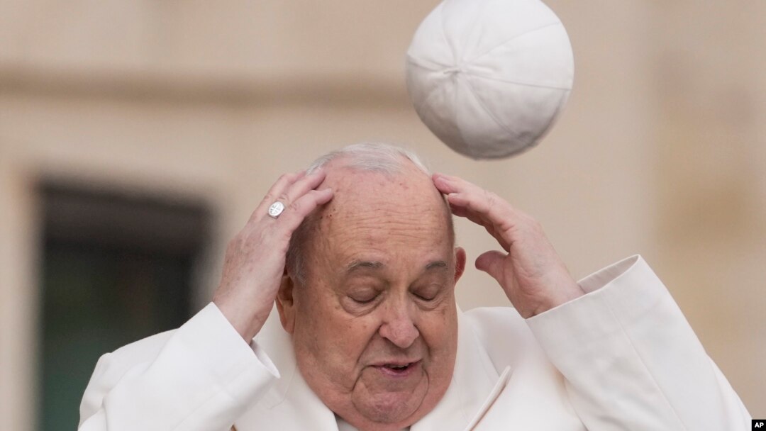 El papa Francisco intenta agarrar su gorra cuando el viento se la lleva mientras llega a su audiencia general semanal en la Plaza de San Pedro en el Vaticano, el 13 de marzo de 2024.