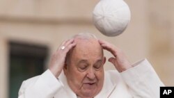 El papa Francisco intenta agarrar su gorra cuando el viento se la lleva mientras llega a su audiencia general semanal en la Plaza de San Pedro en el Vaticano, el 13 de marzo de 2024.