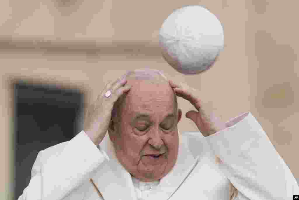 Pope Francis tries to catch his cap as wind blew it away while arriving for his weekly general audience in the St. Peter&#39;s Square at the Vatican.