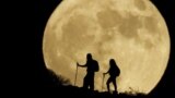 Women walk up a mountain with the full moon known as the "Sturgeon Moon" in the background, in Arguineguin, in the island of Gran Canaria, Spain, Aug. 1, 2023. 