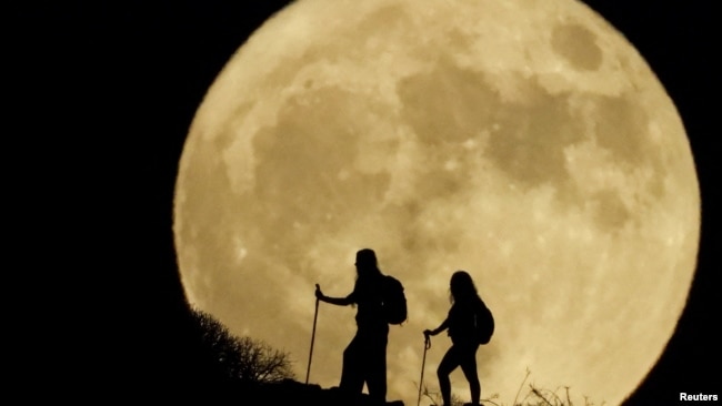 FILE - Women walk up a mountain with the full moon known as the
