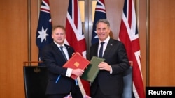 Menteri Pertahanan Inggris Grant Shapps (kiri) dan Menteri Pertahanan Australia Richard Marles bertukar dokumen Perjanjian Pertahanan dalam pertemuan di Gedung Parlemen di Canberra, 21 Maret 2024. (AAP Image/Lukas Coch via Reuters)