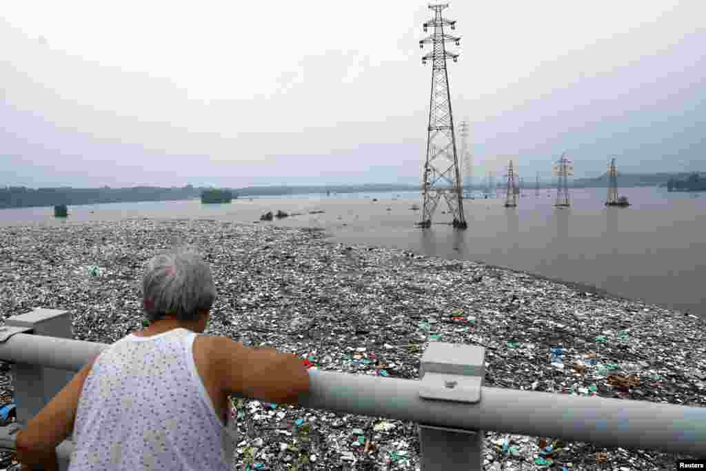 Едно лице гледа во огромен куп ѓубре на поплавена река откако остатоците од тајфунот Доксури донесоа дождови и поплави во Пекинг, Кина.