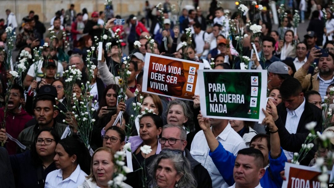 Manifestantes sostienen flores y carteles durante un evento para recordar a los exguerrilleros y líderes sociales asesinados después de la firma de un acuerdo de paz en 2016, en Bogotá, Colombia, el martes 20 de febrero de 2024. 
