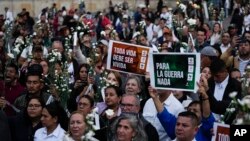 Manifestantes sostienen flores y carteles durante un evento para recordar a los exguerrilleros y líderes sociales asesinados después de la firma de un acuerdo de paz en 2016, en Bogotá, Colombia, el martes 20 de febrero de 2024. 