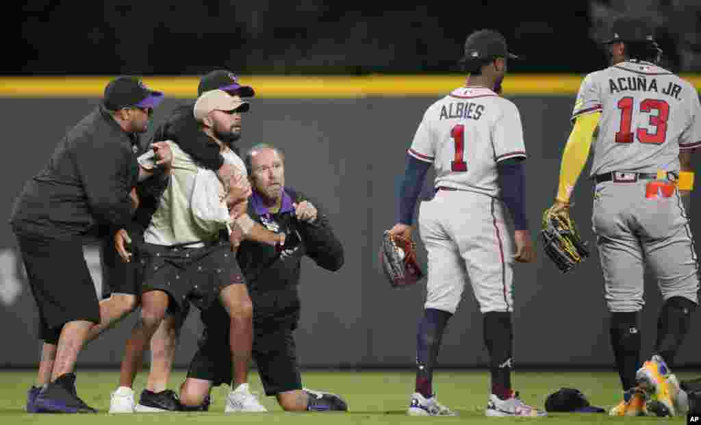 Field guards hold onto a fan as he tries to reach Atlanta Braves right fielder Ronald Acuna Jr., right, while second baseman Ozzie Albies (1) looks on in the seventh inning of a baseball game against the Colorado Rockies, Aug. 28, 2023, in Denver, Coloardo.