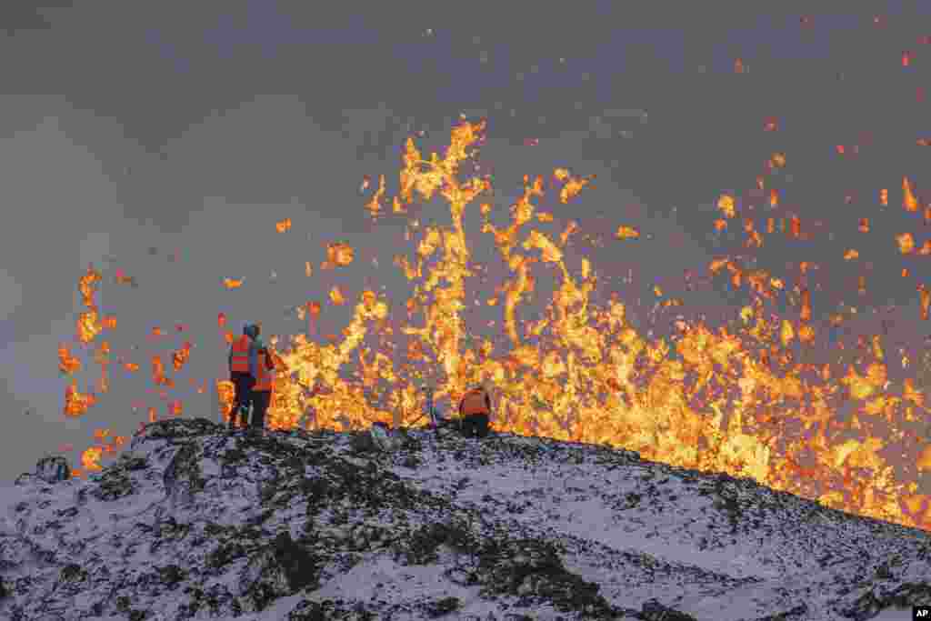 Scientists from the University of Iceland take measurements and samples standing on the ridge in front of the active part of the eruptive fissure of an active volcano in Grindavik on Iceland&#39;s Reykjanes Peninsula, Dec. 19, 2023.