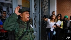 A National Guard officer addresses voters lining up at the Andres Bello School as opposition poll watchers argue they are not being allowed to enter the voting center during the presidential elections in Caracas, Venezuela.