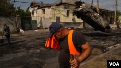 City workers clear debris from cars destroyed by a Russian rocket attack in downtown Kupiansk, leaving at least 10 people wounded, on Aug. 21, 2023. (Yan Boechat/VOA)