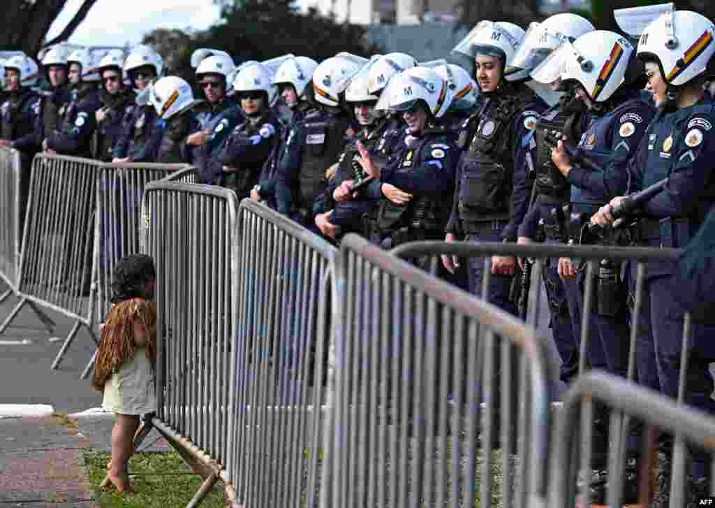 An indigenous boy talks to police officers standing guard as indigenous people taking part in the Terra Livre Indigenous camp, focused on bringing awareness for indigenous rights and land issues and promoting their culture, protest outside the Congress building in Brasilia, April 24, 2023.