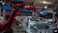 FILE - Visitors look at the robotic arms assembly a vehicle frame during the annual World Robot Conference at the Etrong International Exhibition and Convention Center in the outskirt of Beijing, Aug. 17, 2023. 