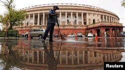 FILE - India's parliament building is reflected in a puddle after the rain as a man sweeps the water in New Delhi, India, July 20, 2018.