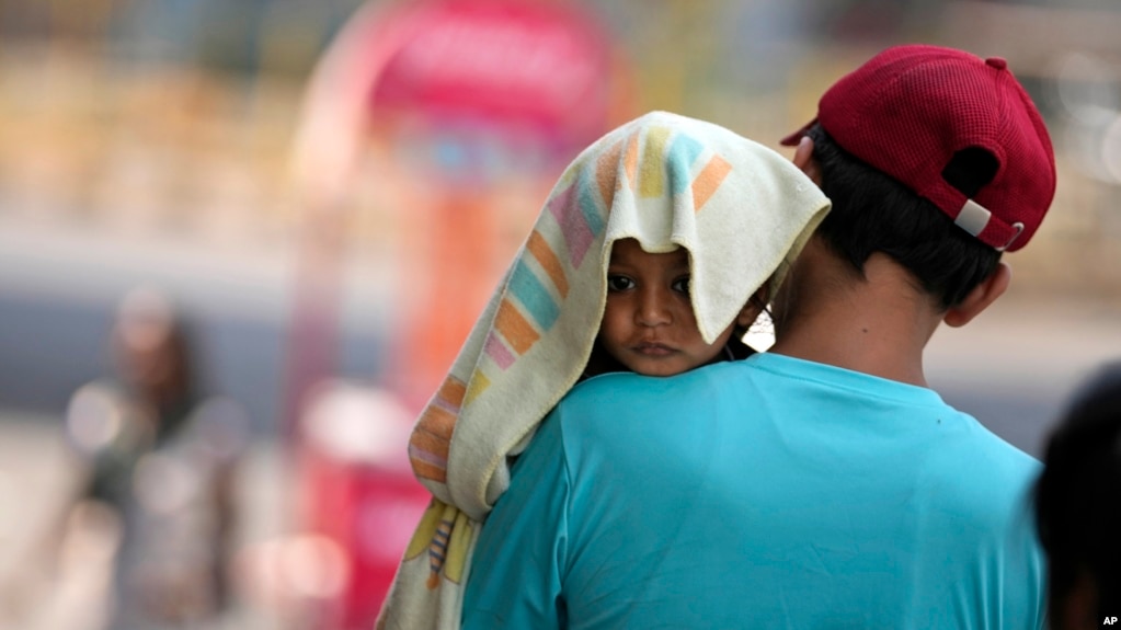 A man carries a child with its head covered with a towel to protect it from the heat in Jammu, India, Sunday, June 2, 2024. (AP Photo/Channi Anand)