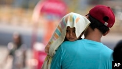 A man carries a child with its head covered with a towel to protect it from the heat in Jammu, India, Sunday, June 2, 2024. (AP Photo/Channi Anand)
