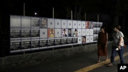 FILE - People walk by an election poster board for Tokyo gubernatorial election in Tokyo, on June 20, 2024.