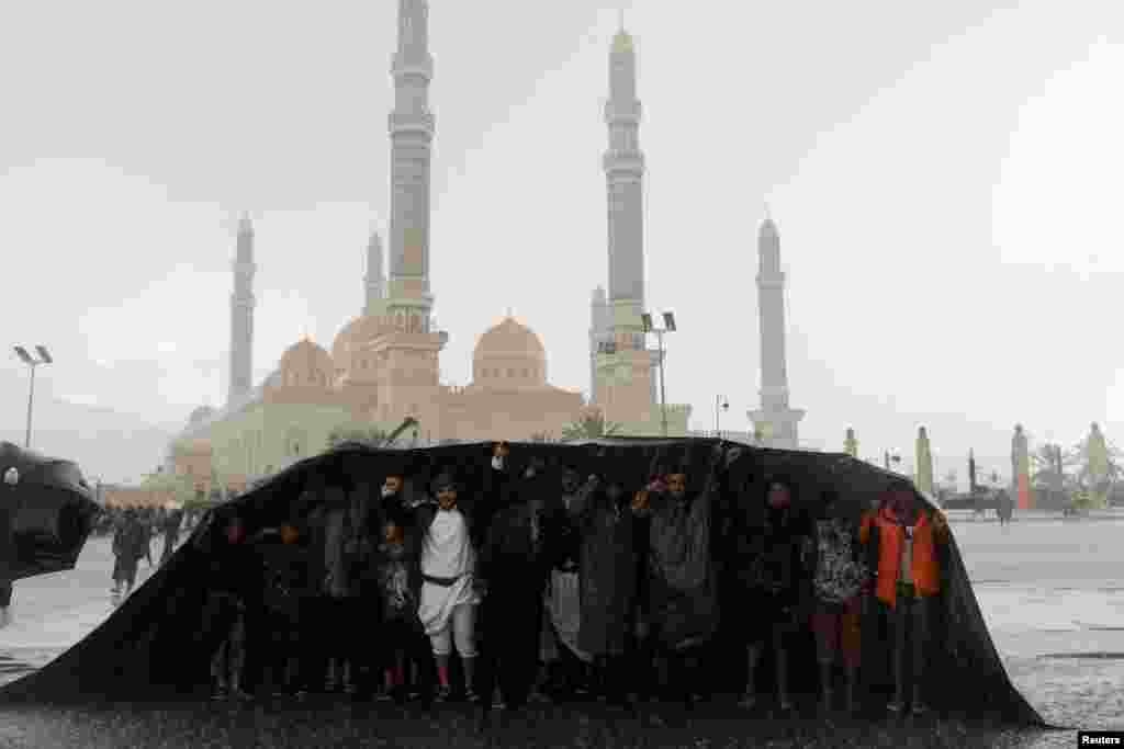 People cover themselves as protesters, mainly Houthi supporters, gather for a rally to show solidarity with Palestinians in the Gaza Strip, during heavy rains, in Sanaa, Yemen.