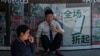 一名男子蹲坐在北京一座商业楼张贴的打折广告前。(2024年5月27日)