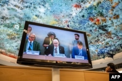 UN High Commissioner for Human Rights Volker Turk, center, is seen on a TV monitor speaking during a session of the 52nd U.N. Human Rights Council, in Geneva, on March 6, 2023.