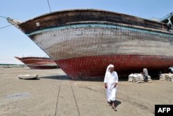 A man walks in front of traditional wooden ships — called lenjes — brought ashore for restoration on Iran's Qeshm island, on April 29, 2023.