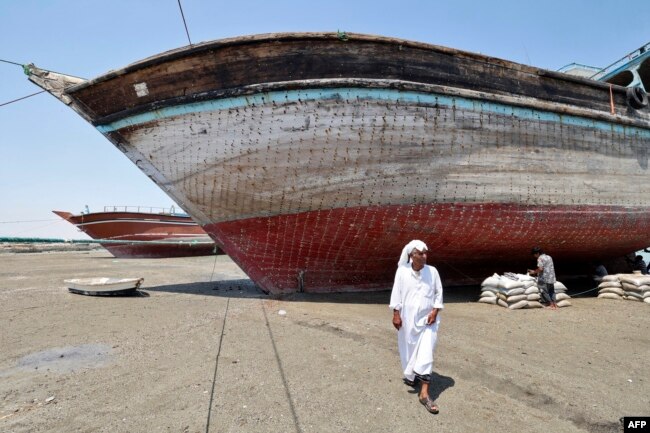 A man walks in front of traditional wooden ships — called lenjes — brought ashore for restoration on Iran's Qeshm island, on April 29, 2023.