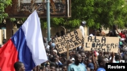 Demonstrators hold a Russian flag and banners during a rally in support of coup soldiers, in Niamey, Niger, July 30, 2023. The signs read "Down with France and its allies" and "Down with imperialism." 