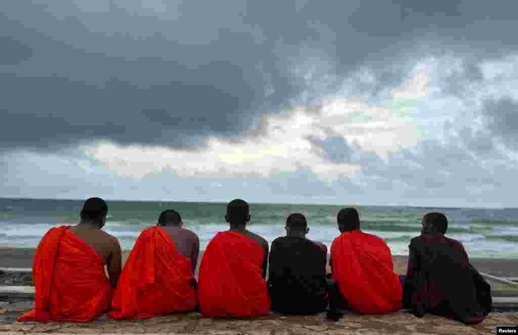 Buddhist monks sit at a beach as rain clouds gather above during the monsoon season, in Colombo, Sri Lanka.