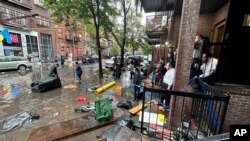 Moradores observam trabalhadores a tentar desobstruir um esgoto nas águas das cheias, sexta-feira, 29 de setembro de 2023, no bairro de Brooklyn, em Nova Iorque.