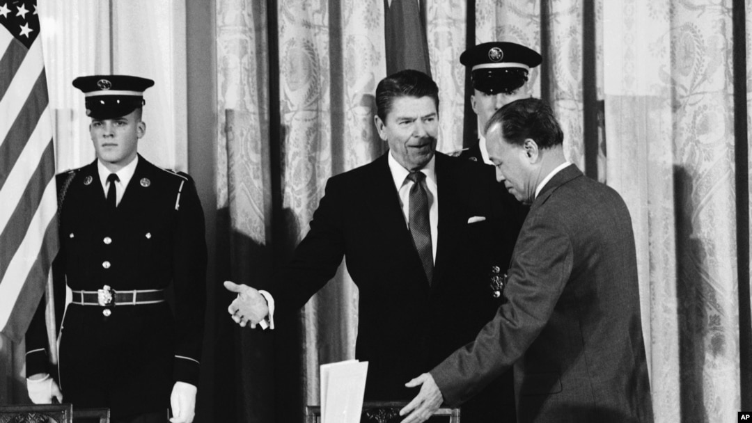 资料照片：1984年1月12日，时任美国总统里根在白宫西厅向时任中国总理赵紫阳示意在签署美中科技协议之前就座。（美联社照片）