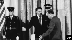 资料照片：1984年1月12日，时任美国总统里根在白宫西厅向时任中国总理赵紫阳示意在签署美中科技协议之前就座。（美联社照片）