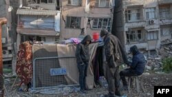 Sejumlah warga yang tedampak gempa dahsyat di Turki dan Suriah berdiri dekat tenda pengungsian yang didirikan dekat gedung yang roboh di Hatay, Turki, 15 Februari 2023. (Foto: Bulent Kilic/AFP)