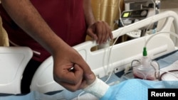 Seorang ayah memegang tangan anaknya yang terluka, Tawfik Abu Youssef, yang dirawat di Rumah Sakit Martir Al-Aqsa pasca serangan Israel di Deir Al-Balah, Jalur Gaza tengah. (Reuters)