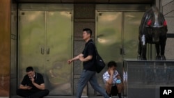 北京一家商场外的一头铜牛和路过的行人与看手机的工人。（2023年5月15日）