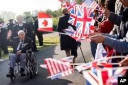 People wave flags for World War II veterans before a ceremony at the Pegasus Bridge memorial in Benouville, Normandy, June 5, 2023.