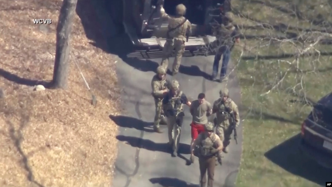 This image made from video provided by WCVB-TV shows Jack Teixeira, in T-shirt and shorts, being taken into custody by armed tactical agents on April 13, 2023, in Dighton, Mass.