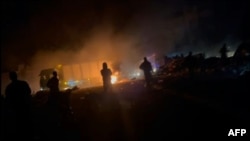 In this image taken from video, trucks move quickly past burning debris near an aid distribution point in Gaza City in pre-dawn darkness as people shout and gunfire echoes on March 30, 2024. The Palestine Red Crescent said five people were killed during the aid delivery.