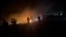In this image taken from video, trucks move quickly past burning debris near an aid distribution point in Gaza City in pre-dawn darkness as people shout and gunfire echoes on March 30, 2024. The Palestine Red Crescent said five people were killed during the aid delivery.