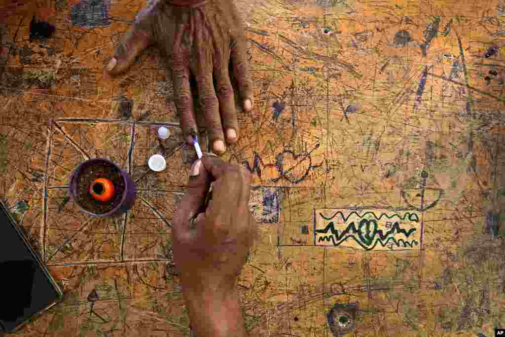 A voter puts his hand on a classroom desk covered in marks as a polling officer applies an indelible ink mark on his index finger at a polling station inside a school during the second round of voting in the national election, near Palakkad, in Indian southern state of Kerala.