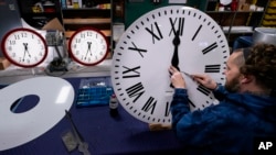 Ian Roders fastens the hands to a clock at Electric Time Company, Tuesday, Nov. 1, 2022, in Medfield, Mass. (AP Photo/Charles Krupa)