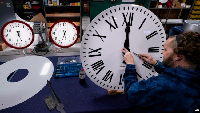 Ian Roders fastens the hands to a clock at Electric Time Company, Tuesday, Nov. 1, 2022, in Medfield, Mass. (AP Photo/Charles Krupa)