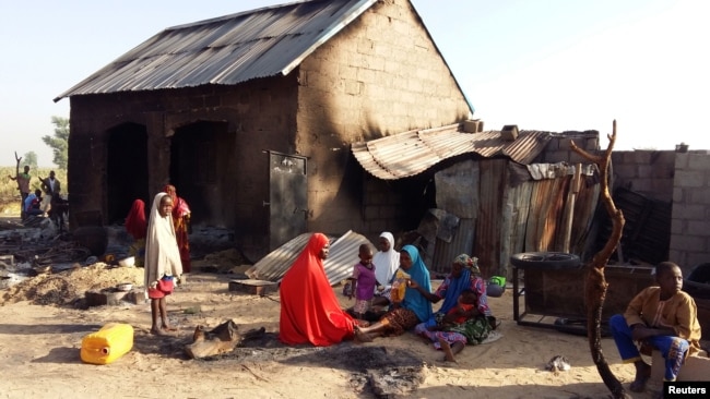 FILE - People sit near a burned house after an attack by suspected members of the Islamist Boko Haram militant group, in Bulabulin village, Nigeria, Nov. 1, 2018.