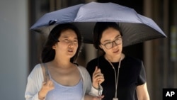 People use an umbrella to shield themselves from the sun as they walk along a street on an unseasonably hot day in Beijing, June 24, 2023. 